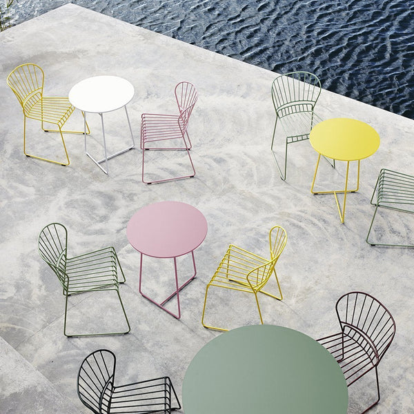 Colorful metal chairs and tables in pastel shades of yellow, pink, green, and white against a textured gray surface.