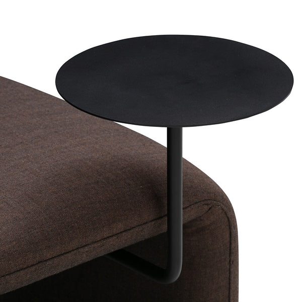 Black round accent table with sleek design, contrasting a rich brown sofa fabric for modern appeal.