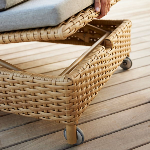 Light brown woven rattan with smooth texture; wheels for mobility on a wooden deck surface.