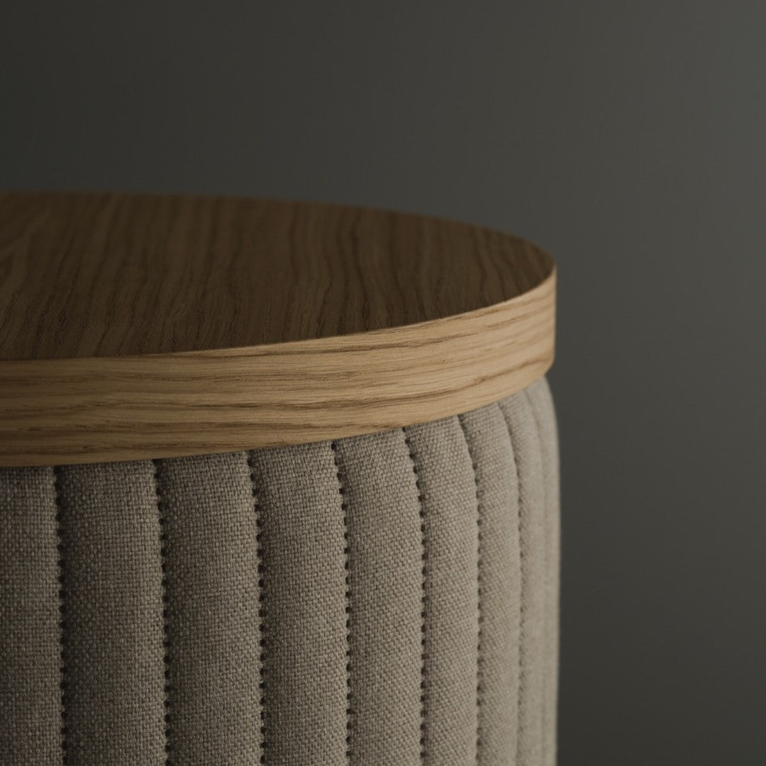 Beige upholstered stool with vertical ribbed pattern and light wooden top against a dark gray background.