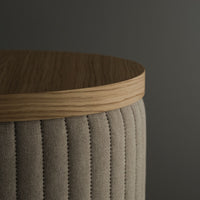 Beige upholstered stool with vertical ribbed pattern and light wooden top against a dark gray background.