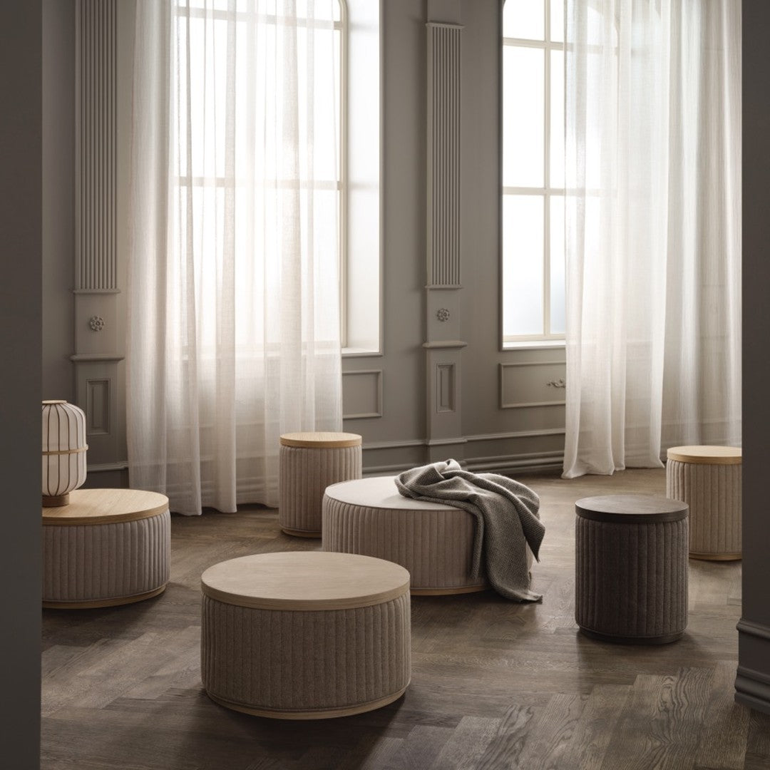 Neutral-toned round ottomans with subtle ribbed patterns, complementing a soft, airy space with sheer white curtains.
