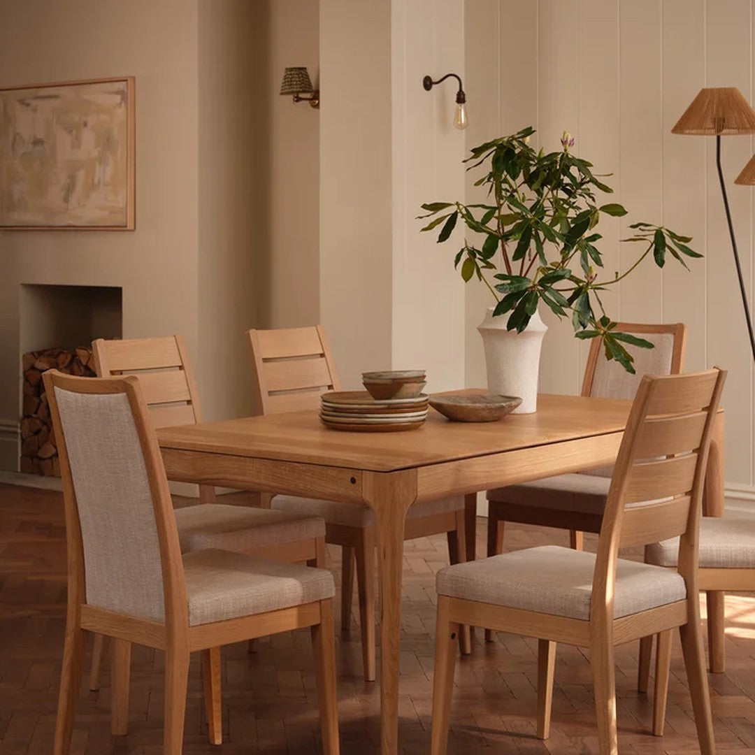 Natural wood dining table with beige and tan accents, featuring neutral tones and soft textures in a cozy setting.