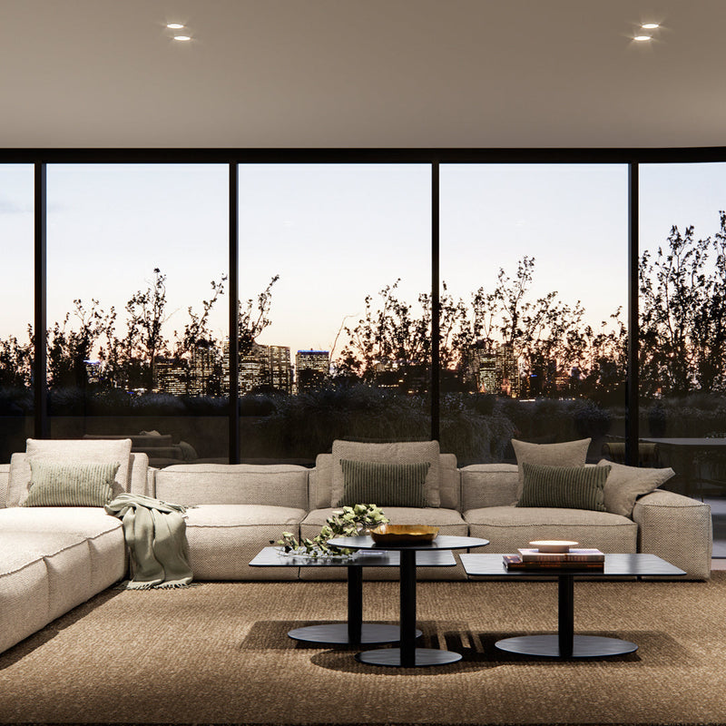 Light beige sectional sofa with green accents, black glass coffee tables, and natural woven rug in a modern living room.
