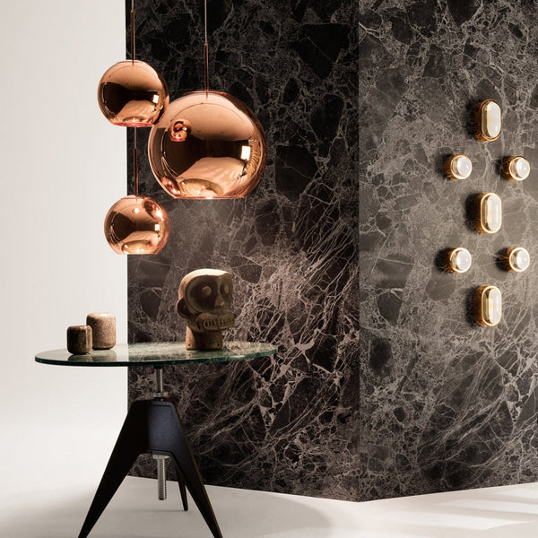 Copper pendant lights hang over a sleek glass table against a textured black marble wall with gold accents.