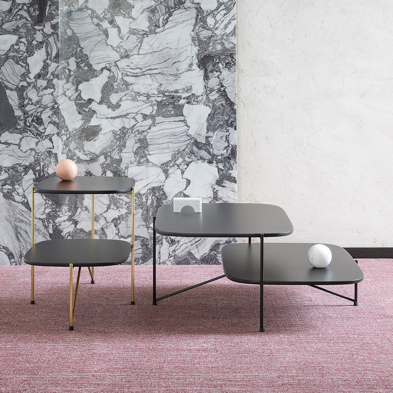 Modern black coffee and side tables with gold accents, set against a marble-patterned wall and pink textured rug.