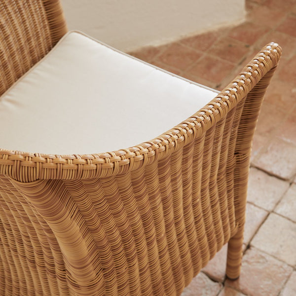 Natural brown woven rattan chair with a crisp white cushion on a textured tiled floor.