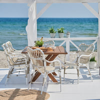 "White wicker dining chairs with natural wood table, set against a serene ocean backdrop."
