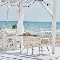 White beach chairs and table with natural wood accents, set against a backdrop of blue ocean and sandy shore.