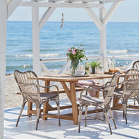 "Light beige wicker chairs, natural wood table, white accents, and vibrant floral centerpiece by the beach."