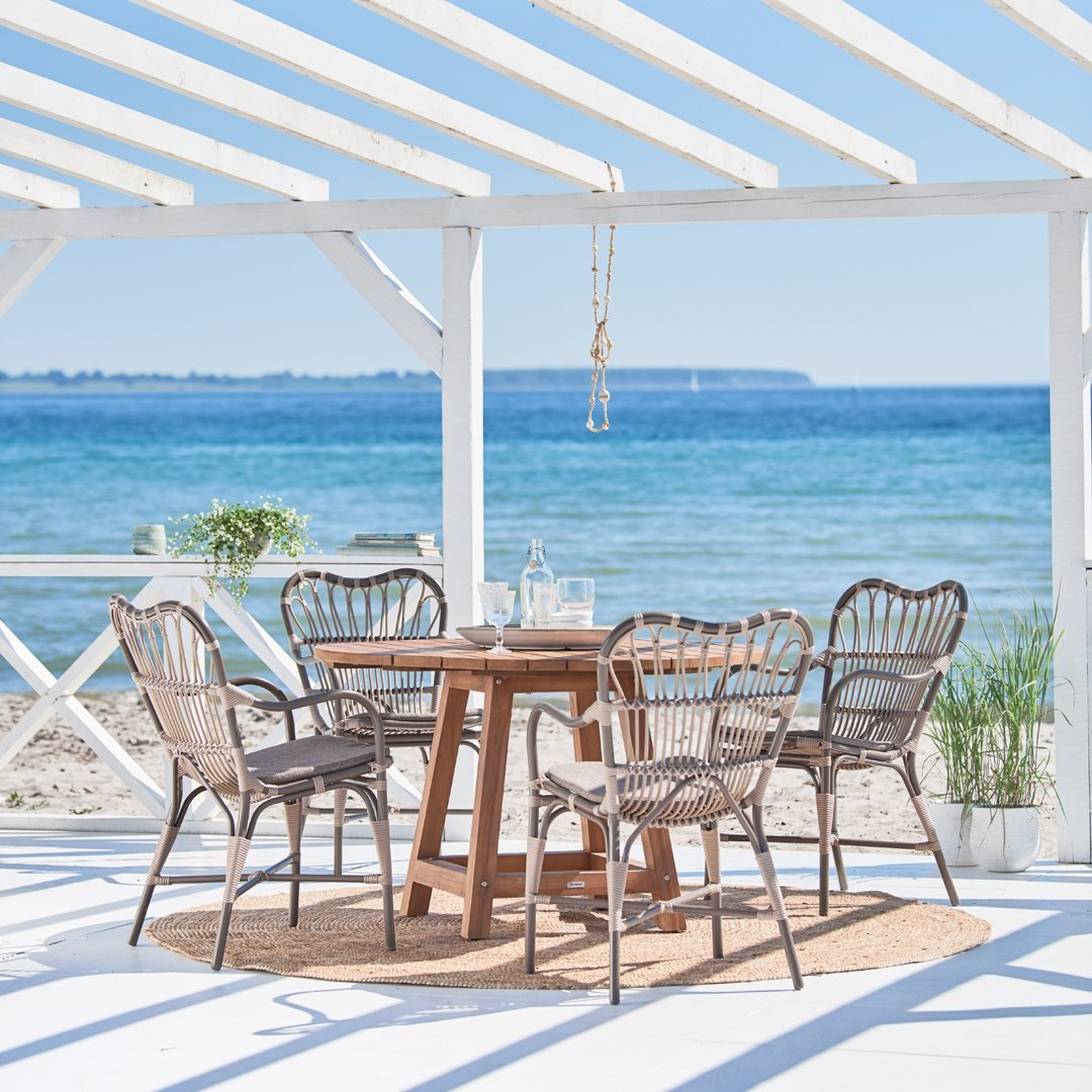 "Coastal-inspired outdoor dining set featuring natural wicker chairs and a rustic wooden table under a bright blue sky."