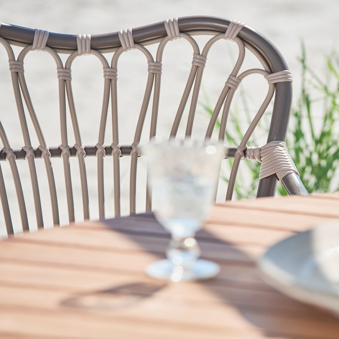 Light beige patio chair with intricate woven pattern, paired with a clear glass, set on a warm wooden table.