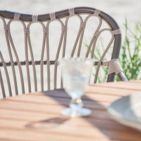 Light beige patio chair with intricate woven pattern, paired with a clear glass, set on a warm wooden table.