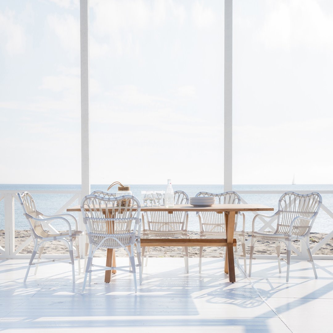 White wicker dining chairs with a wooden table, featuring light coastal tones and soft, airy patterns in a bright setting.