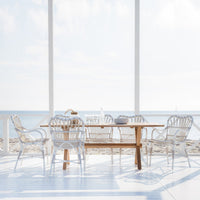 White wicker dining chairs with a wooden table, featuring light coastal tones and soft, airy patterns in a bright setting.