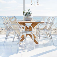 "Elegant white wicker dining chairs around a light wood table, set against a serene beach backdrop with bright blue skies."