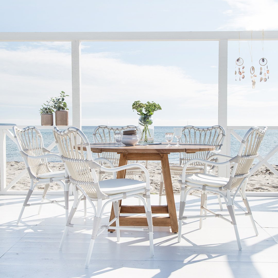Elegant white wicker dining chairs paired with a natural wood table, set against a serene beach backdrop.