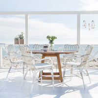 Elegant white wicker dining chairs paired with a natural wood table, set against a serene beach backdrop.