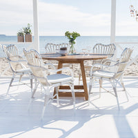 White wicker dining set with blue cushions, featuring a natural wood table, set against a serene beach backdrop.