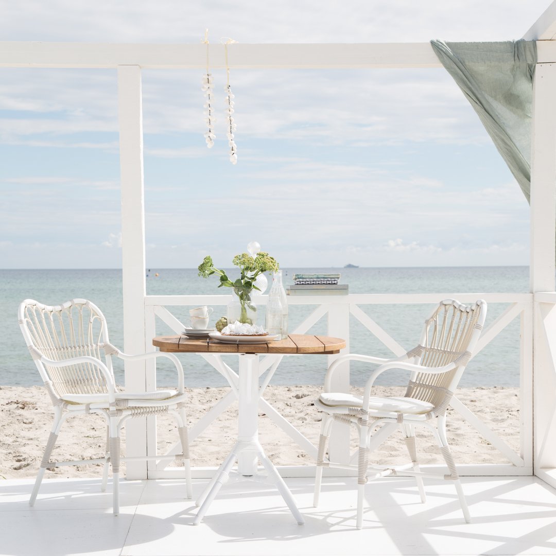 "Coastal dining set with white and beige stripes, natural wood accents, and a light green canopy by the beach."