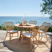 Rattan dining set featuring natural wood tones, white cushions, and a round, woven rug, perfect for outdoor settings.