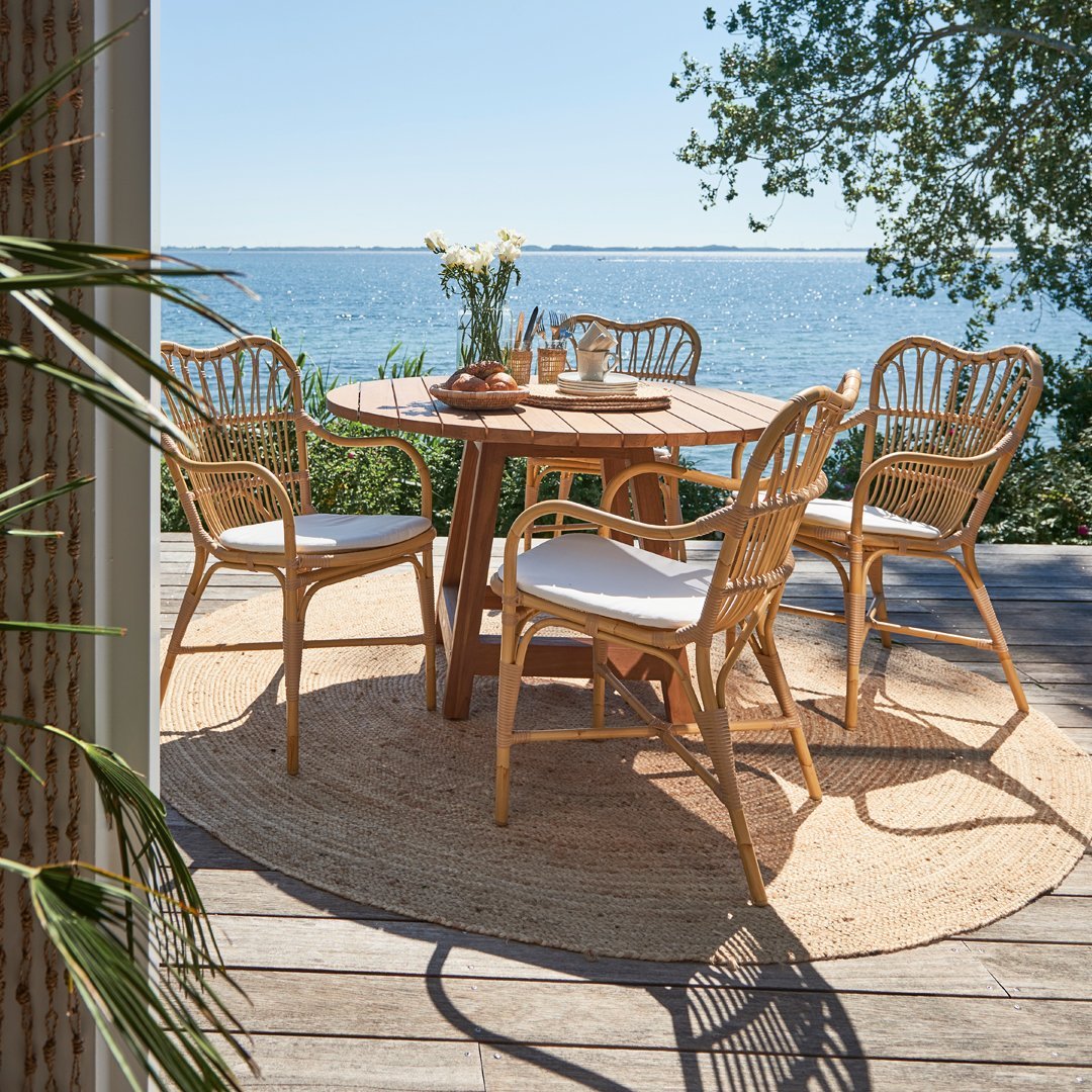 Natural wood tones with woven patterns and light cream cushions on a round table and chairs, complemented by a round jute rug.