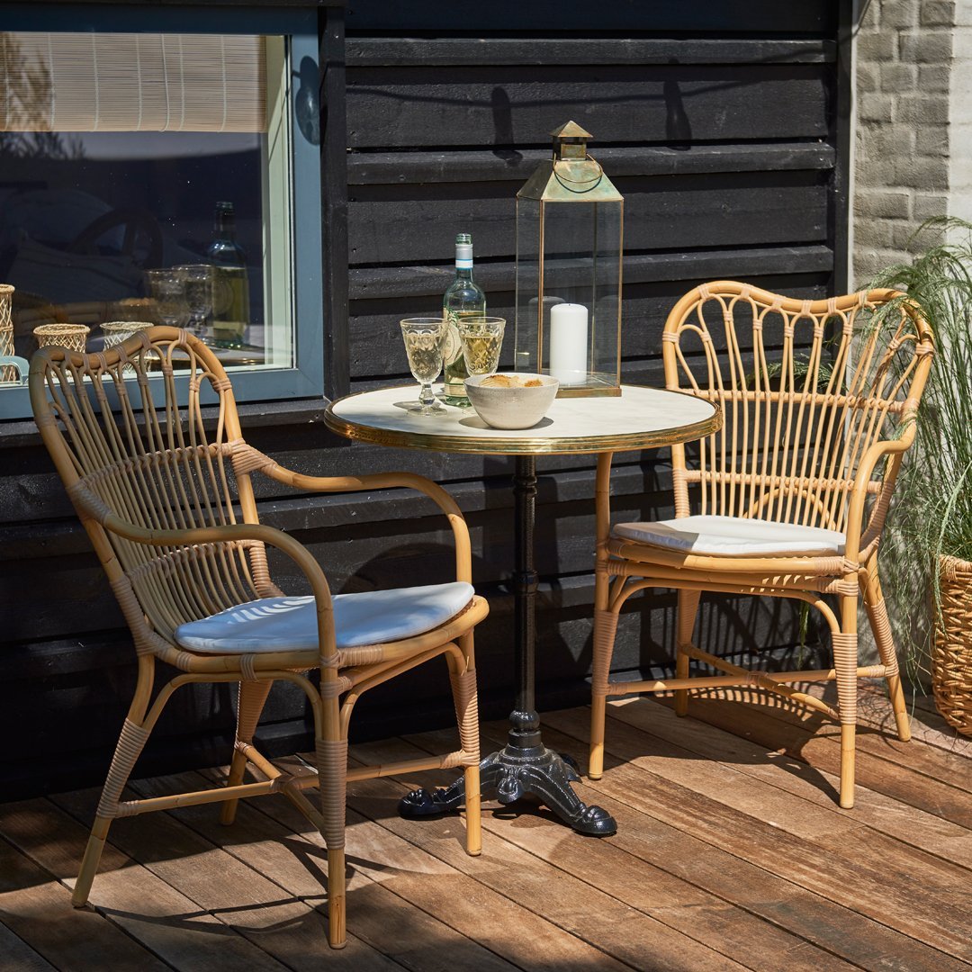 "Natural rattan chairs with light blue cushions and a round white table set against dark wood backdrop."