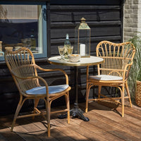 "Natural rattan chairs with light blue cushions and a round white table set against dark wood backdrop."