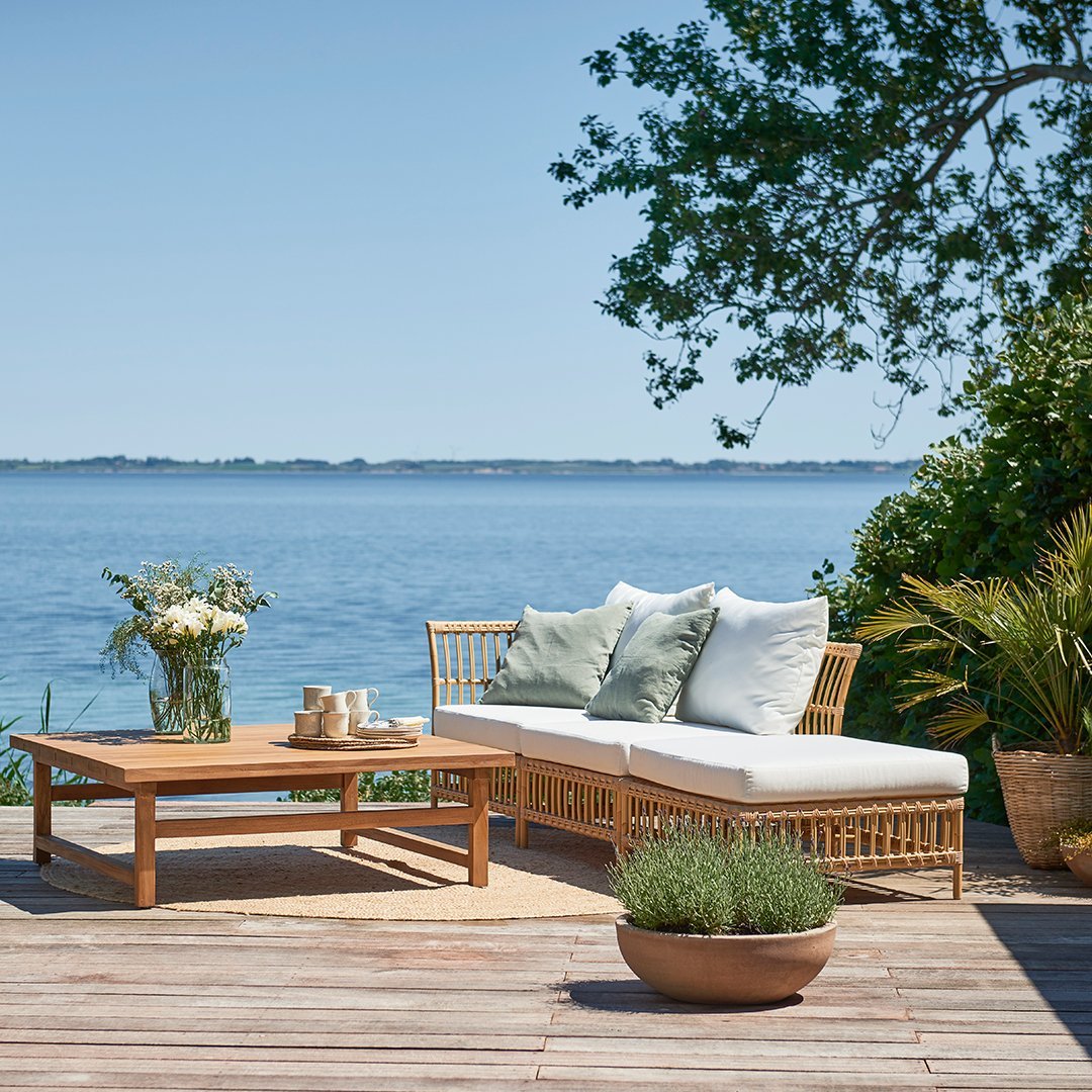 Light beige patio sofa with white cushions and soft green accents, paired with a natural wood coffee table.
