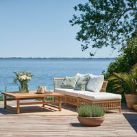 Light beige patio sofa with white cushions and soft green accents, paired with a natural wood coffee table.
