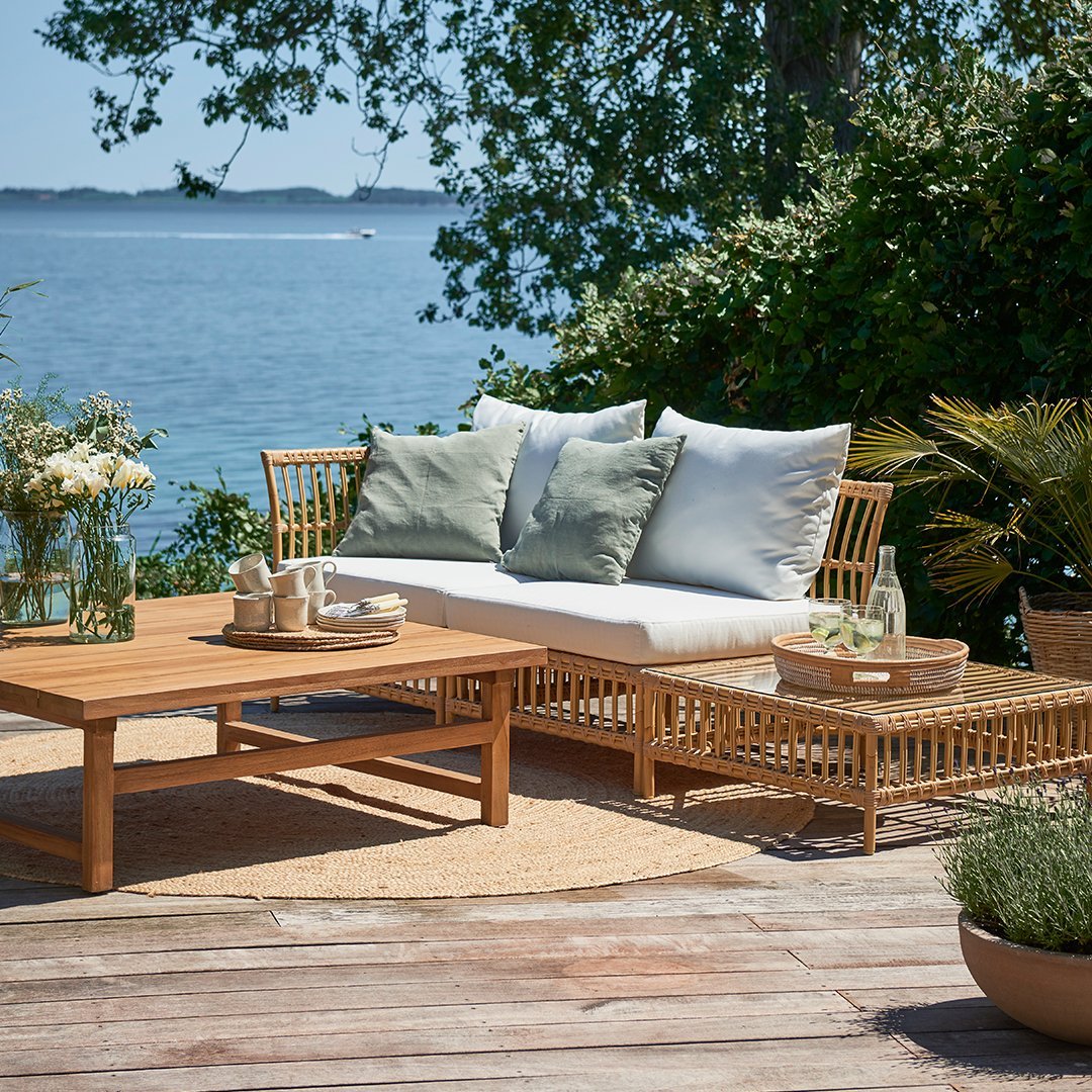 Natural wood tones with soft green and white cushions, complemented by earthy textures and a serene outdoor setting.