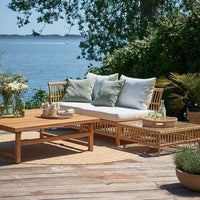 Natural wood tones with soft green and white cushions, complemented by earthy textures and a serene outdoor setting.
