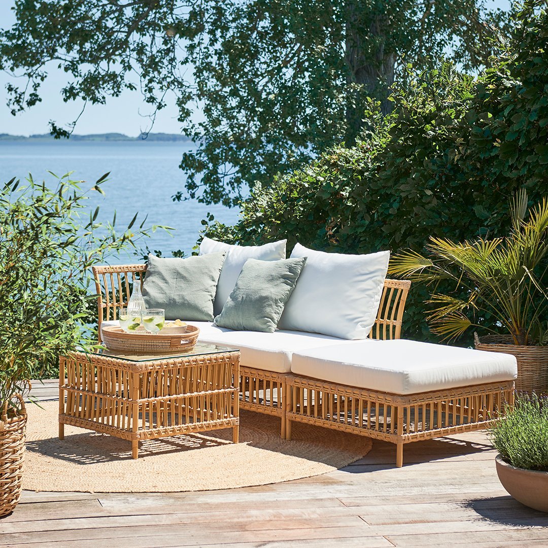 Natural rattan outdoor furniture set with white cushions and green accent pillows on a sunny patio.