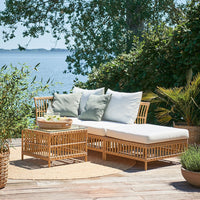 Natural rattan outdoor furniture set with white cushions and green accent pillows on a sunny patio.