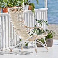 Cream and white woven chair with a modern design, set against a beachside backdrop. Elegant and airy look.