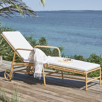 White cushioned lounge chair with natural rattan frame, set against a serene blue ocean backdrop. 