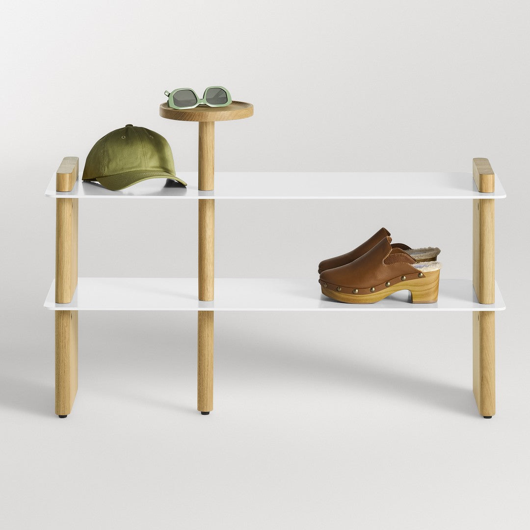 White shelf unit with oak legs, featuring a green cap, round wood table, and brown clogs. Simple and modern design.