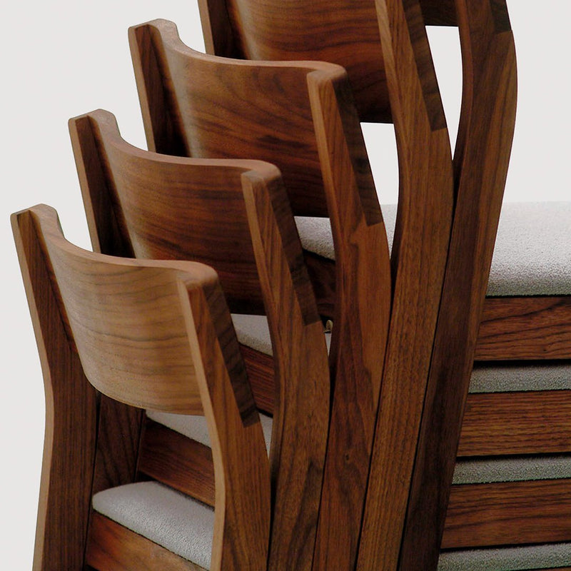 "Stacked wooden chairs with a rich brown finish and light gray cushioned seats, featuring smooth, sleek lines."
