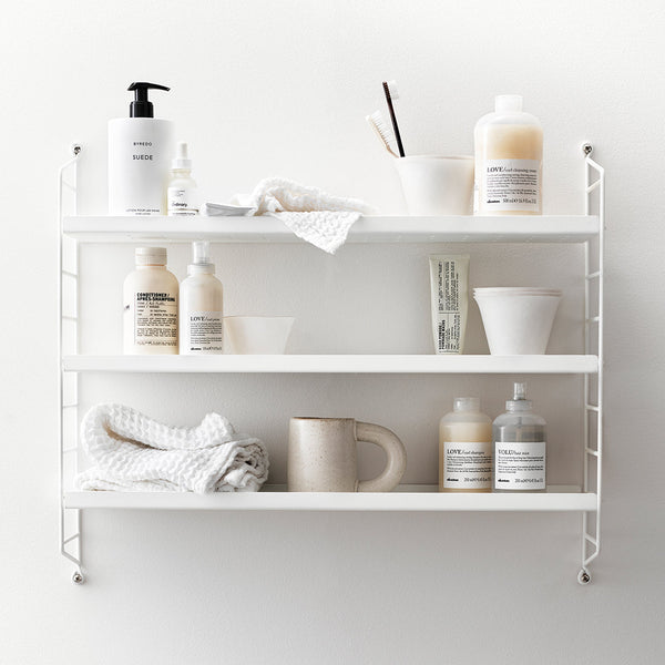 Three-tier white shelving unit displaying beige, cream, and gray containers, with textured white towels and linens.