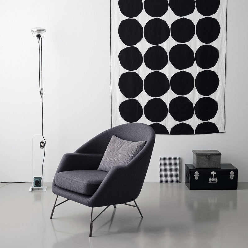 Gray armchair in front of a black and white patterned wall hanging with large circles. Modern minimalist decor.