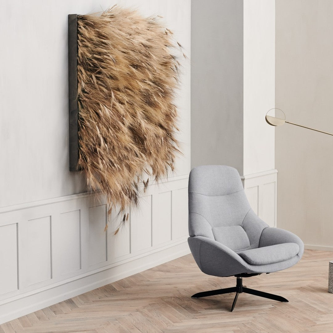 Neutral gray armchair beside a textured, beige wall art piece featuring natural dried grass elements.