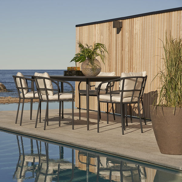 Modern outdoor dining set featuring sleek black frames, soft white cushions, and natural wood accents near a pool.
