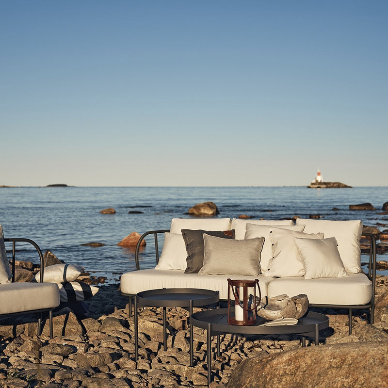 Coastal patio furniture in soft beige and gray tones, featuring minimalist patterns against a serene ocean backdrop.