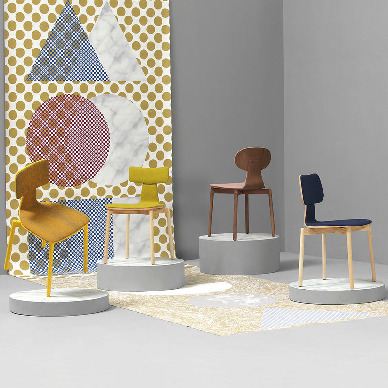 Colorful chairs in yellow, brown, and navy blue, displayed against a geometric patterned backdrop of polka dots and shapes.