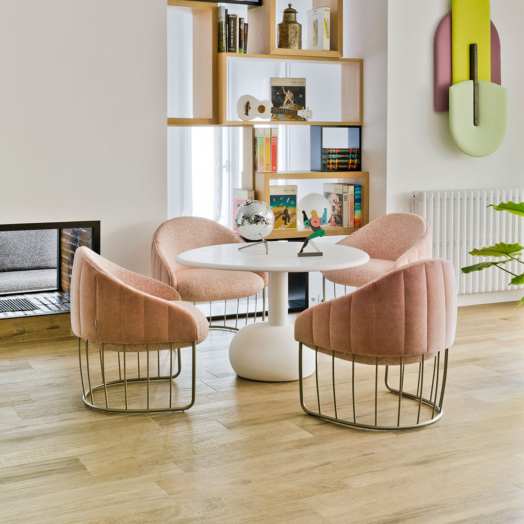 Soft pink velvet chairs with gold wire bases around a round white table in a modern, bright interior.