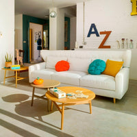 Bright white sofa with colorful cushions in orange, turquoise, and yellow; complemented by wooden coffee tables against a modern backdrop.