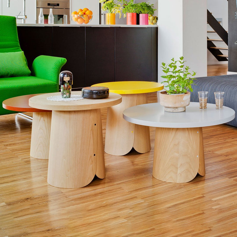 Colorful round coffee tables in white, yellow, orange, and natural wood tones, featuring unique scalloped edges.