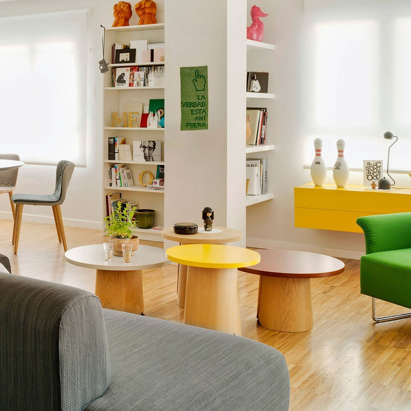 Colorful living room featuring green and yellow accent tables, with light wood floors and neutral gray couch.