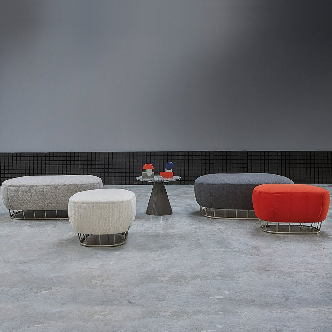 Modern ottomans in gray, white, and vibrant orange, featuring soft textures and round shapes, arranged around a sleek table.