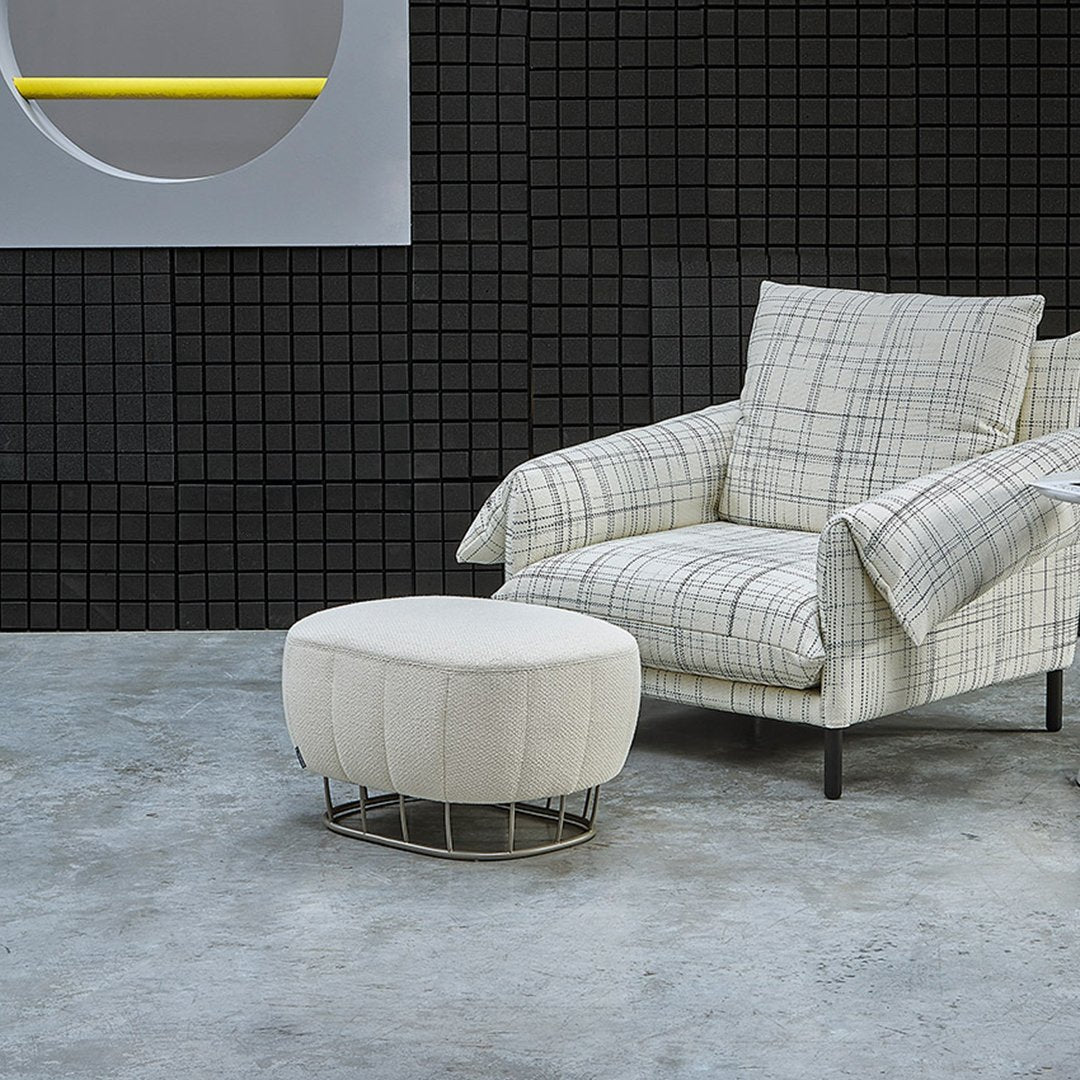 Plaid patterned armchair in gray and white, paired with a textured white ottoman against a modern black grid wall.